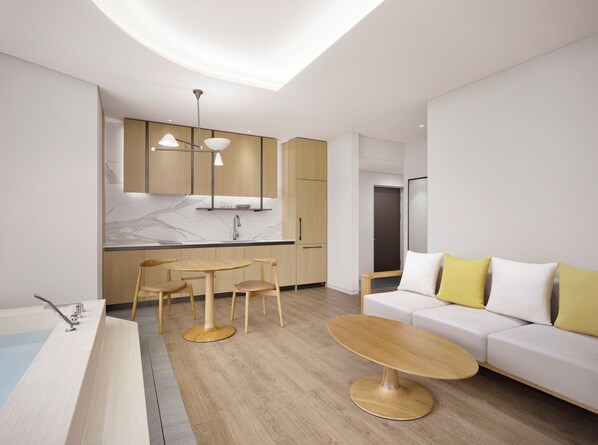 Una sala de estar moderna y bien iluminada, con suelo de madera, una mesa de centro redonda, un sofá con cojines amarillos y una zona de cocina con encimera de mármol y armarios de madera.