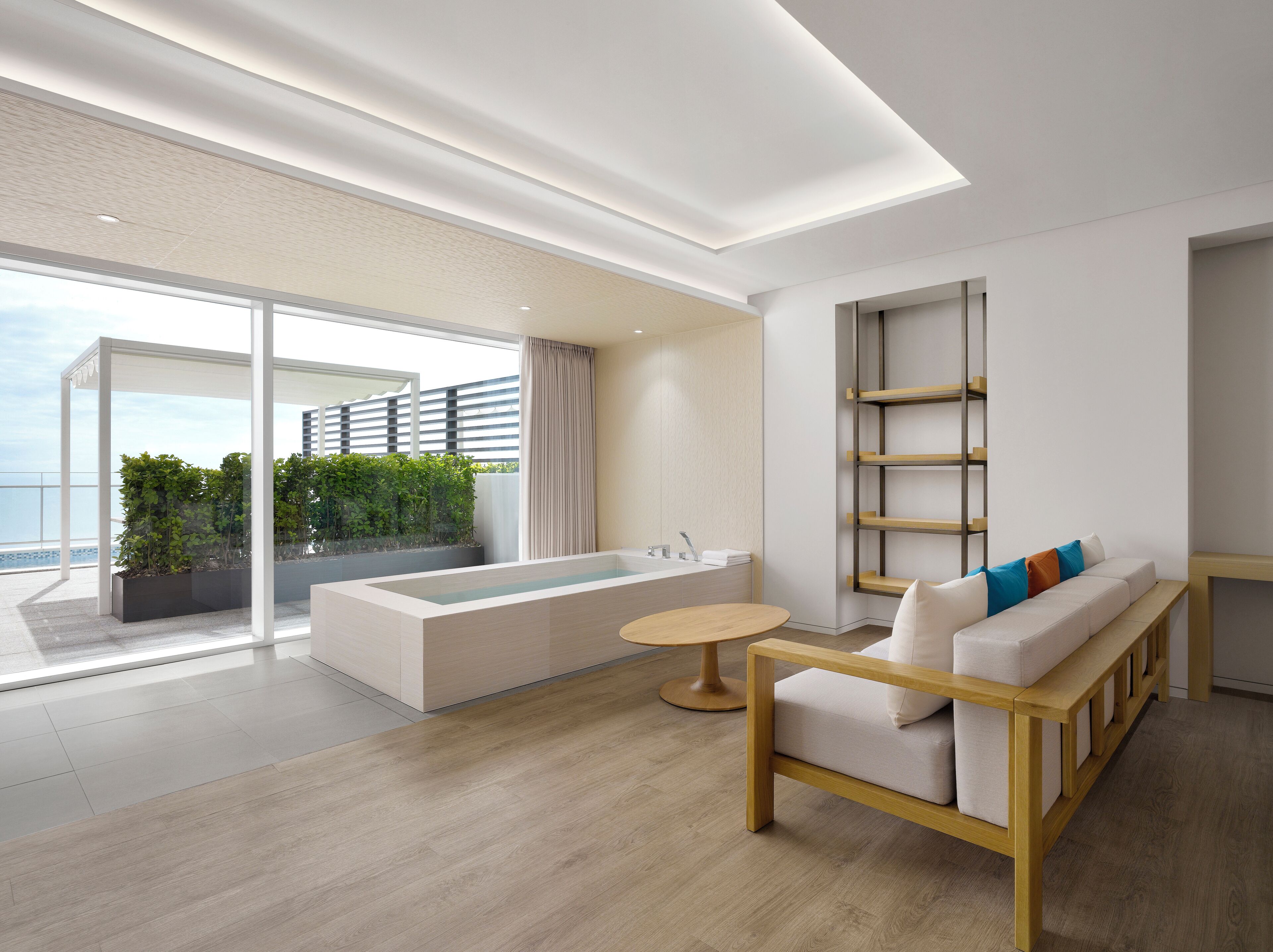 A modern hotel room with a large balcony, a bathtub, a sofa, and a small table.