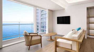 A modern hotel room with a large balcony, a flat-screen TV, and a sofa with cushions.