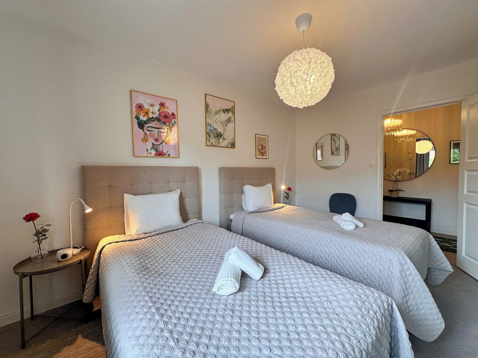 Ett hotellrum med två sängar, en rund kristallkrona och konstverk på väggarna.
