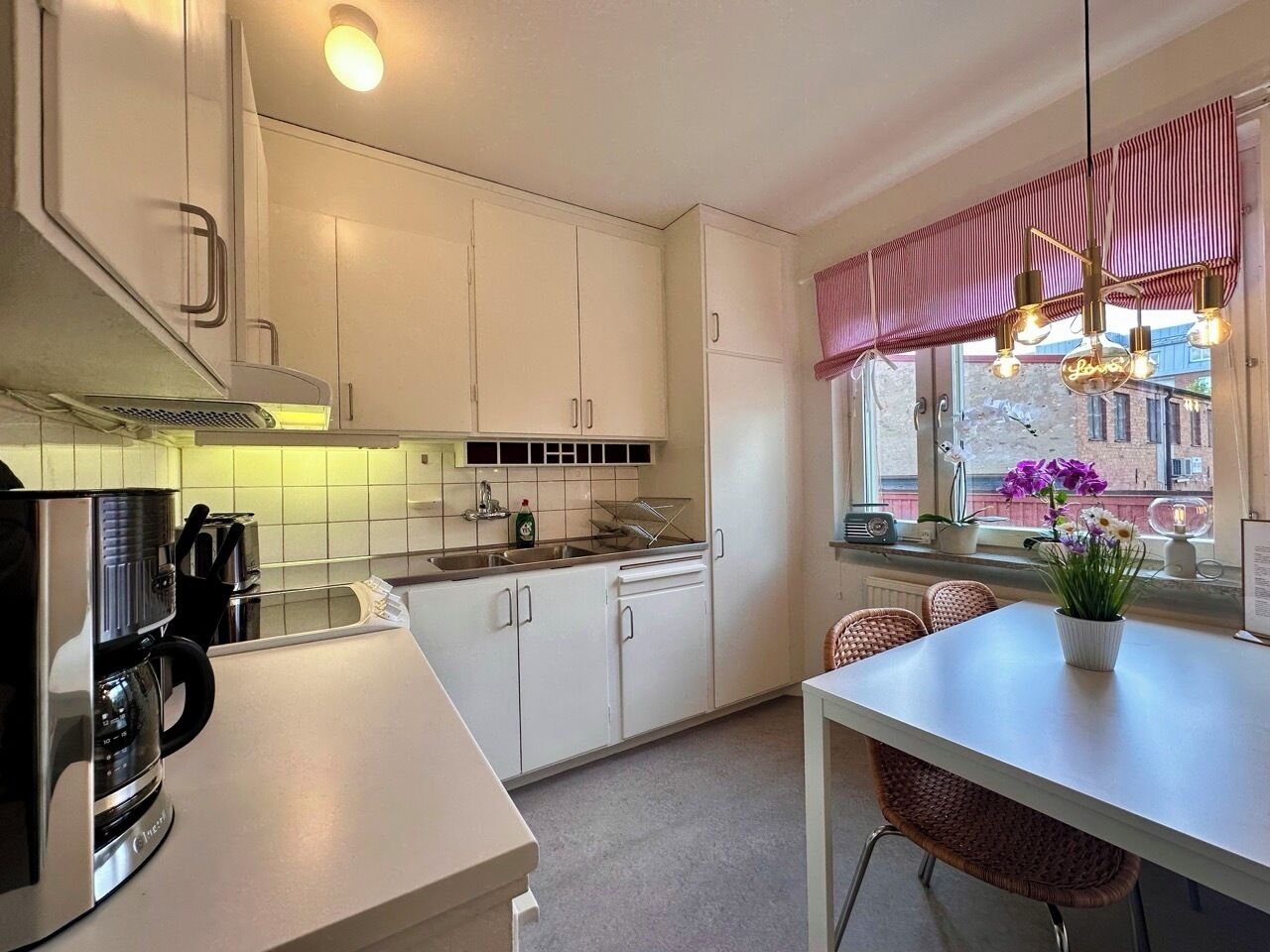 Una cocina moderna con armarios blancos, una cafetera y un comedor con mesa y sillas.