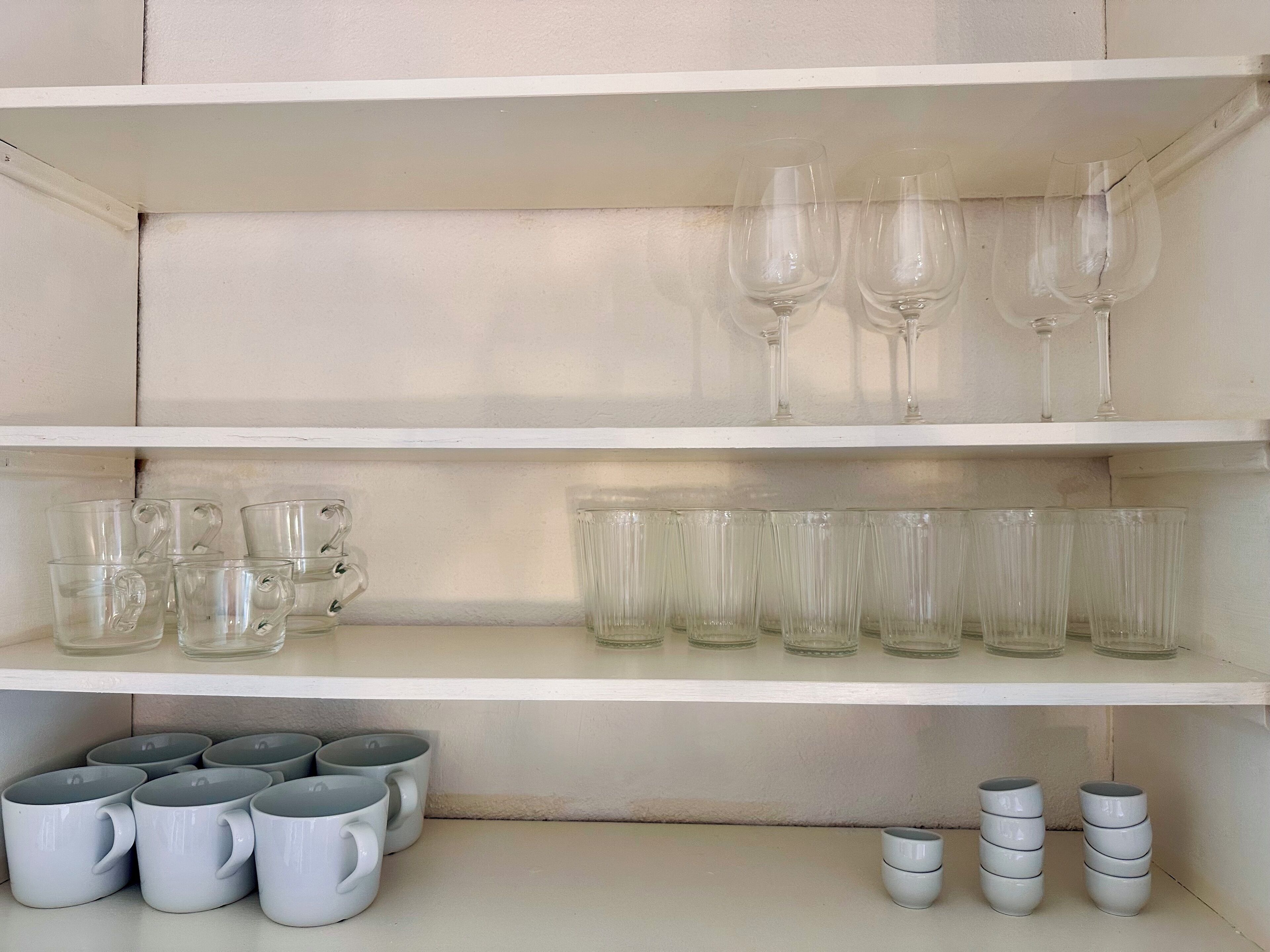 A shelf with various glassware including wine glasses, tumblers, and mugs.