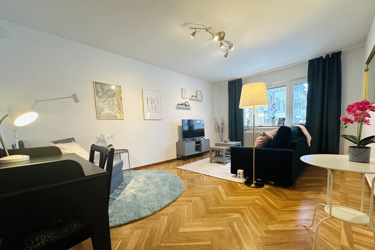Un salon moderne avec un plancher en bois, un canapé noir, une table à manger et un téléviseur.