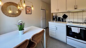 Een moderne keuken met witte kastjes, een wit aanrechtblad, een inbouwoven en een hanglamp.