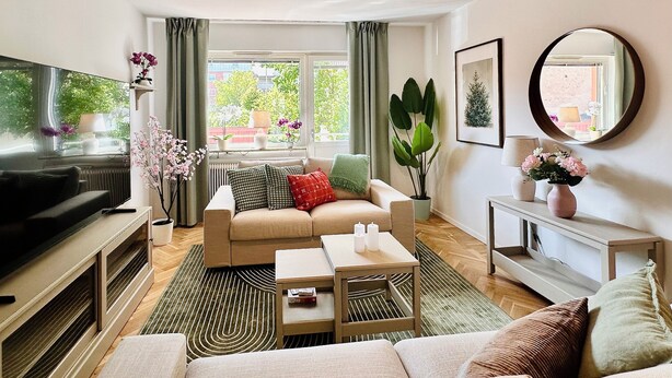 Een moderne woonkamer met een bank, salontafel, televisie en een groot raam met gordijnen.