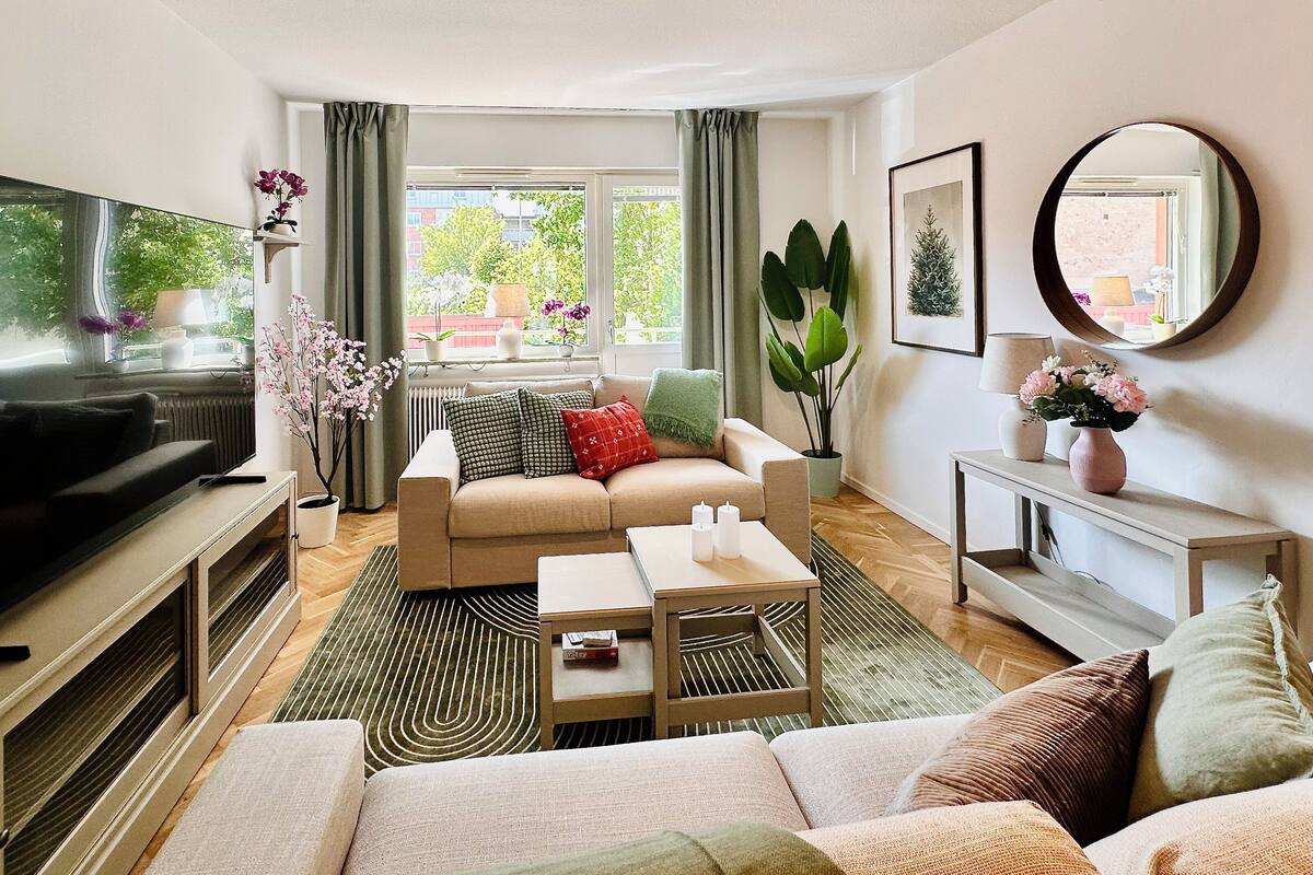 Un salon moderne avec un canapé, une table basse, un téléviseur et une grande fenêtre avec des rideaux.