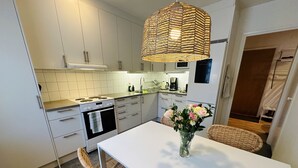 Een moderne keuken met witte kasten, een fornuis en een eethoek met een witte tafel en rieten stoelen.