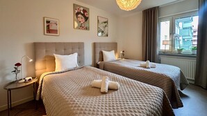 Een hotelkamer met twee bedden, een nachtkastje met een lamp, een raam met gordijnen en kunst aan de muur.