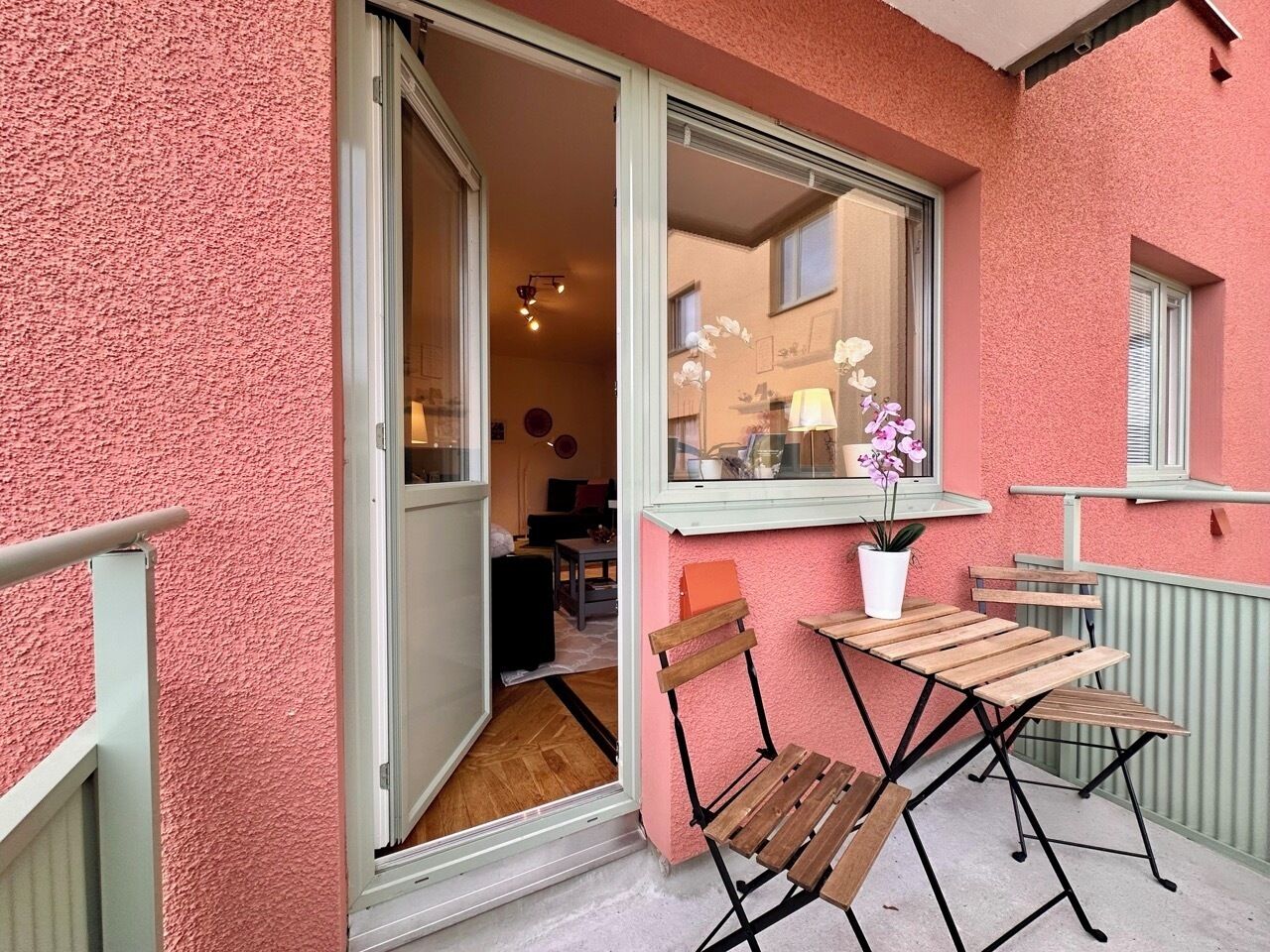 Une porte coulissante ouverte donne sur un espace de vie comprenant une table et des chaises en bois, une plante en pot et une fenêtre offrant une vue sur l’intérieur.