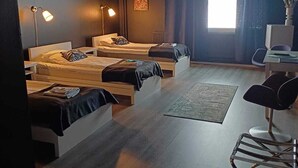 A modern, compact room with three single beds, a desk, and a chair.