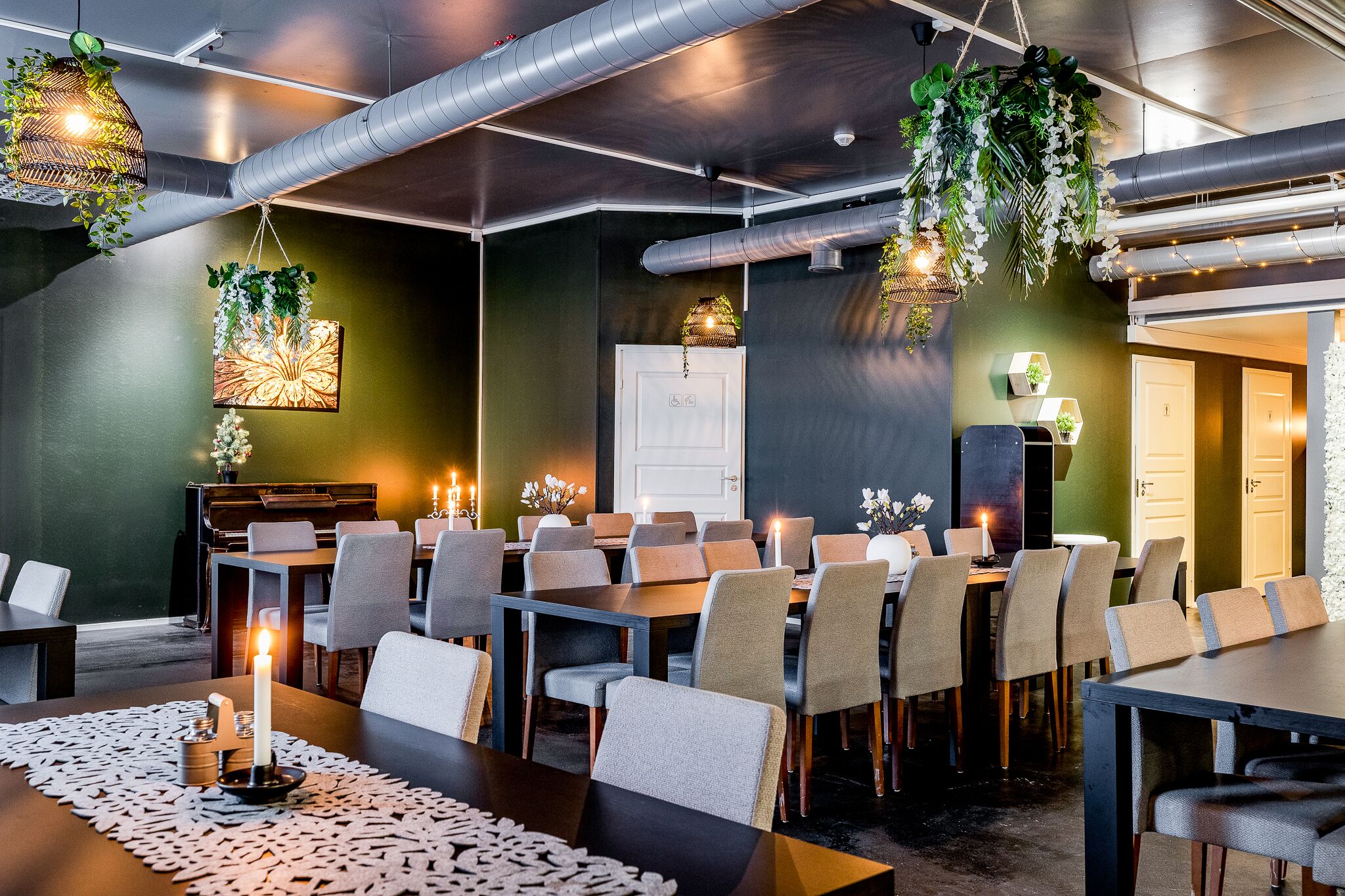 A conference room with multiple tables and chairs, a piano, and hanging plants.