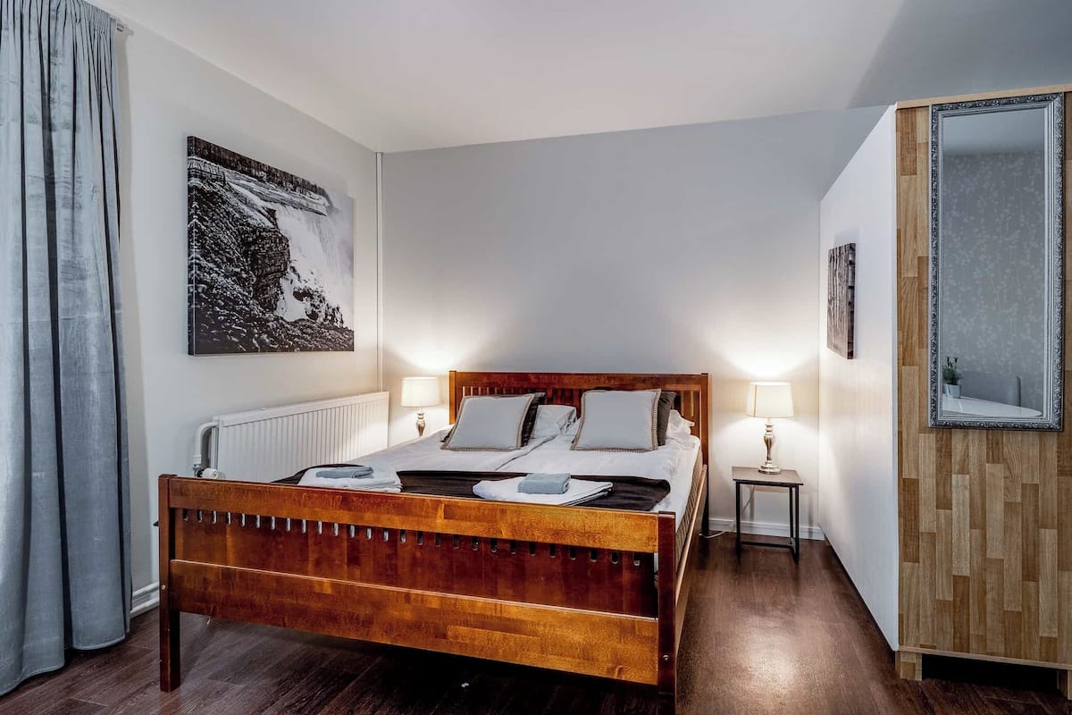 Una cama bien tendida con cabecera de madera, una mesita de noche con lámpara y un cuadro enmarcado en la pared.