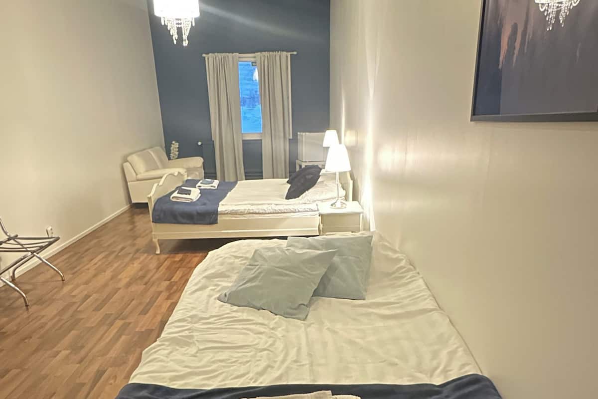 Habitación de hotel con cama, una silla, escritorio, lámpara de escritorio y ventana con cortinas.