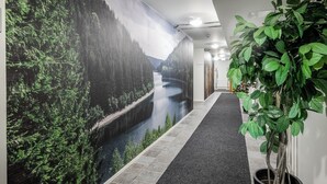 A hallway with a mural of a forest and river, a potted plant, and a carpeted floor.