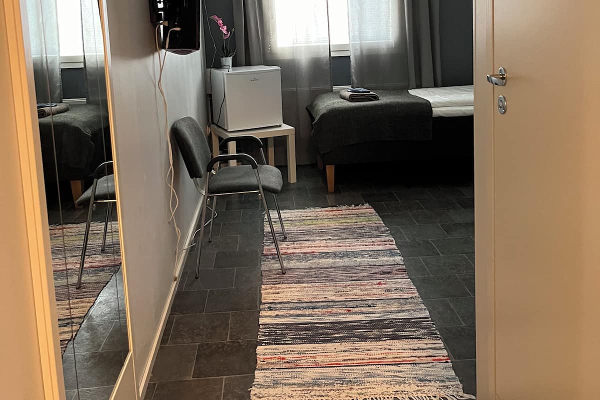 Habitación de hotel compacta con cama, escritorio, silla, espejo y televisor.