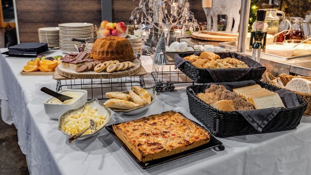 A buffet table with various food items, including a large cake, bread, pastries, and fruits.