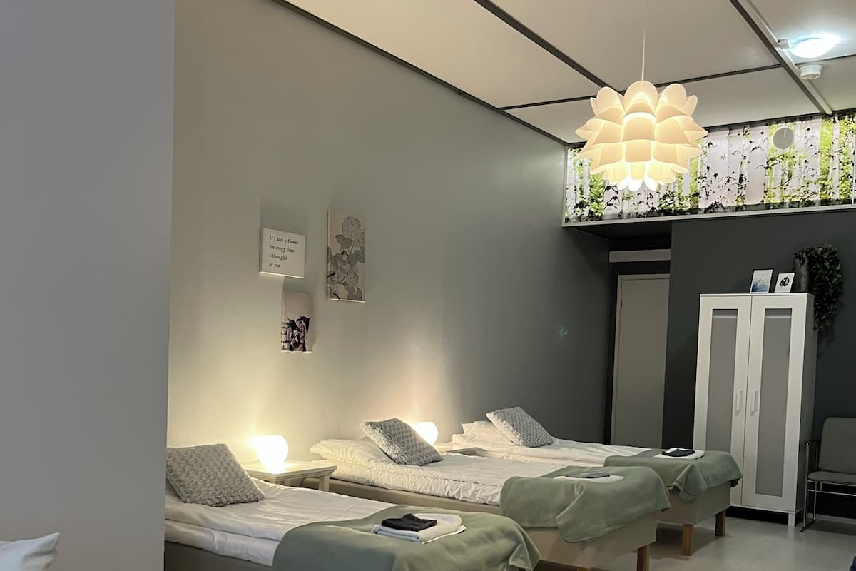 Una habitación de hotel moderna con tres camas individuales, un sofá blanco, una alfombra estampada y un techo con diseño geométrico.