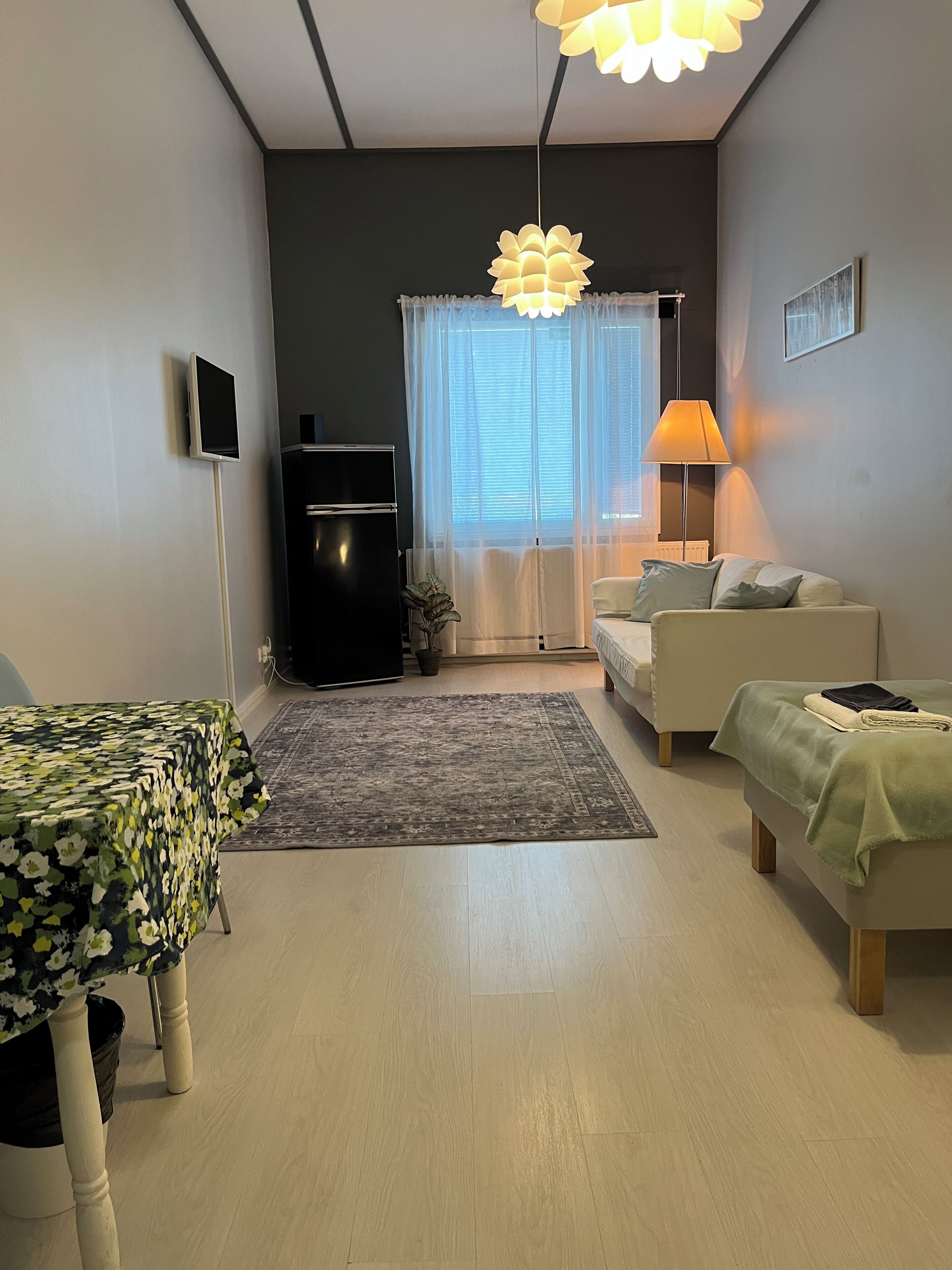 Una sala de estar moderna con un sofá, una mesita, un televisor, una lámpara y un ventanal con cortinas.