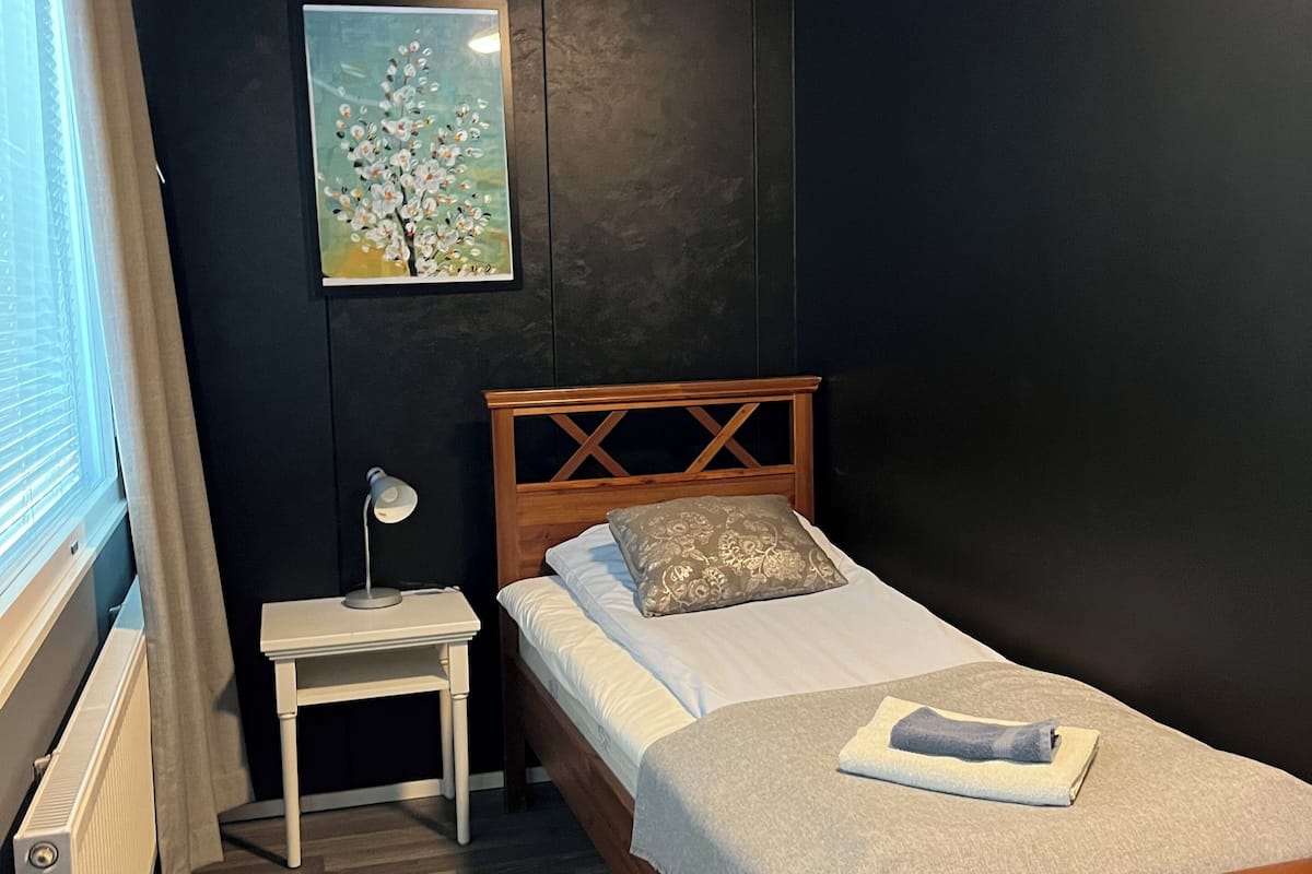 Un dormitorio con cama de madera, una mesita de noche, una lámpara, un radiador y un cuadro en la pared.