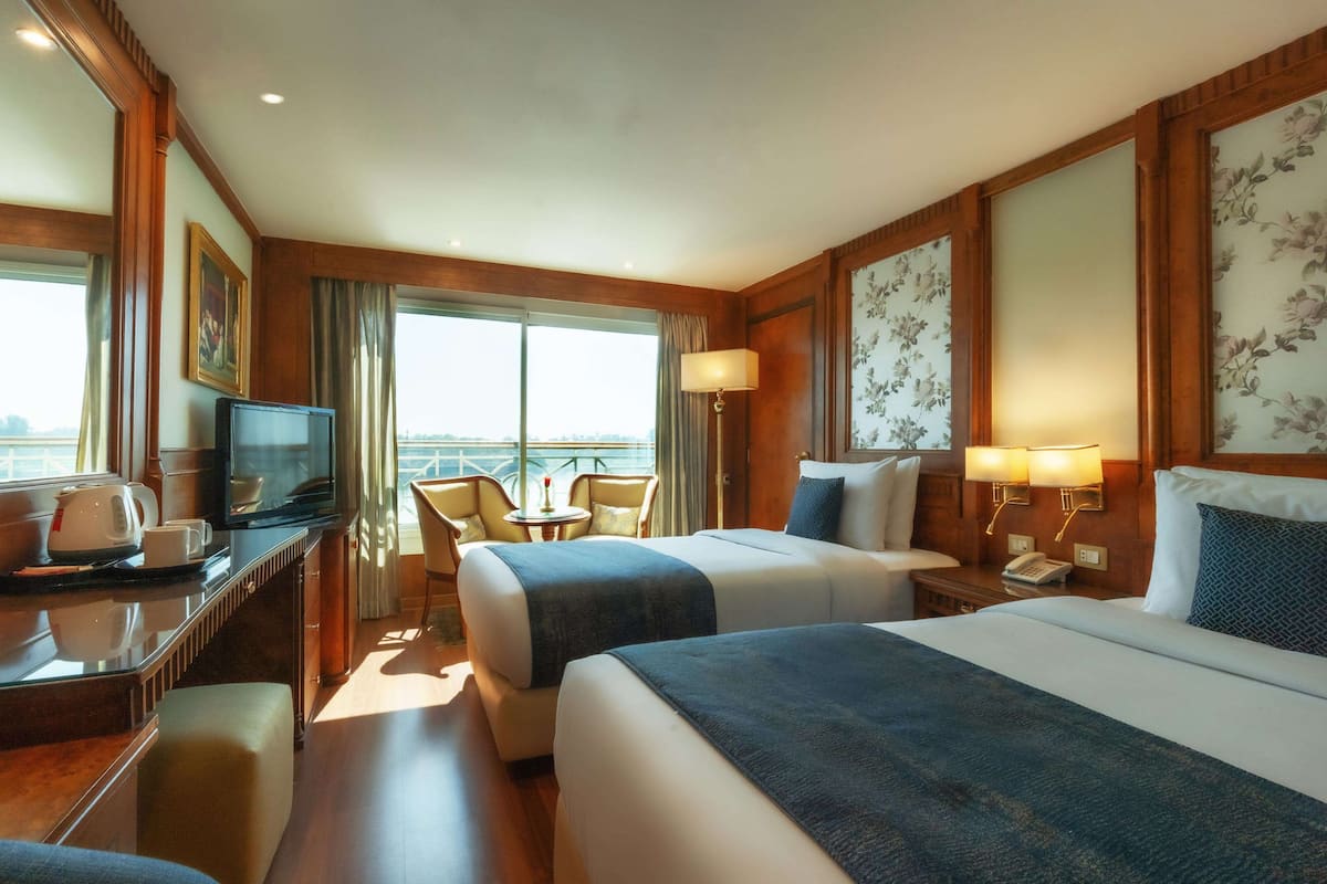 A hotel room with two beds, a desk with a television, a small table, and a chair.