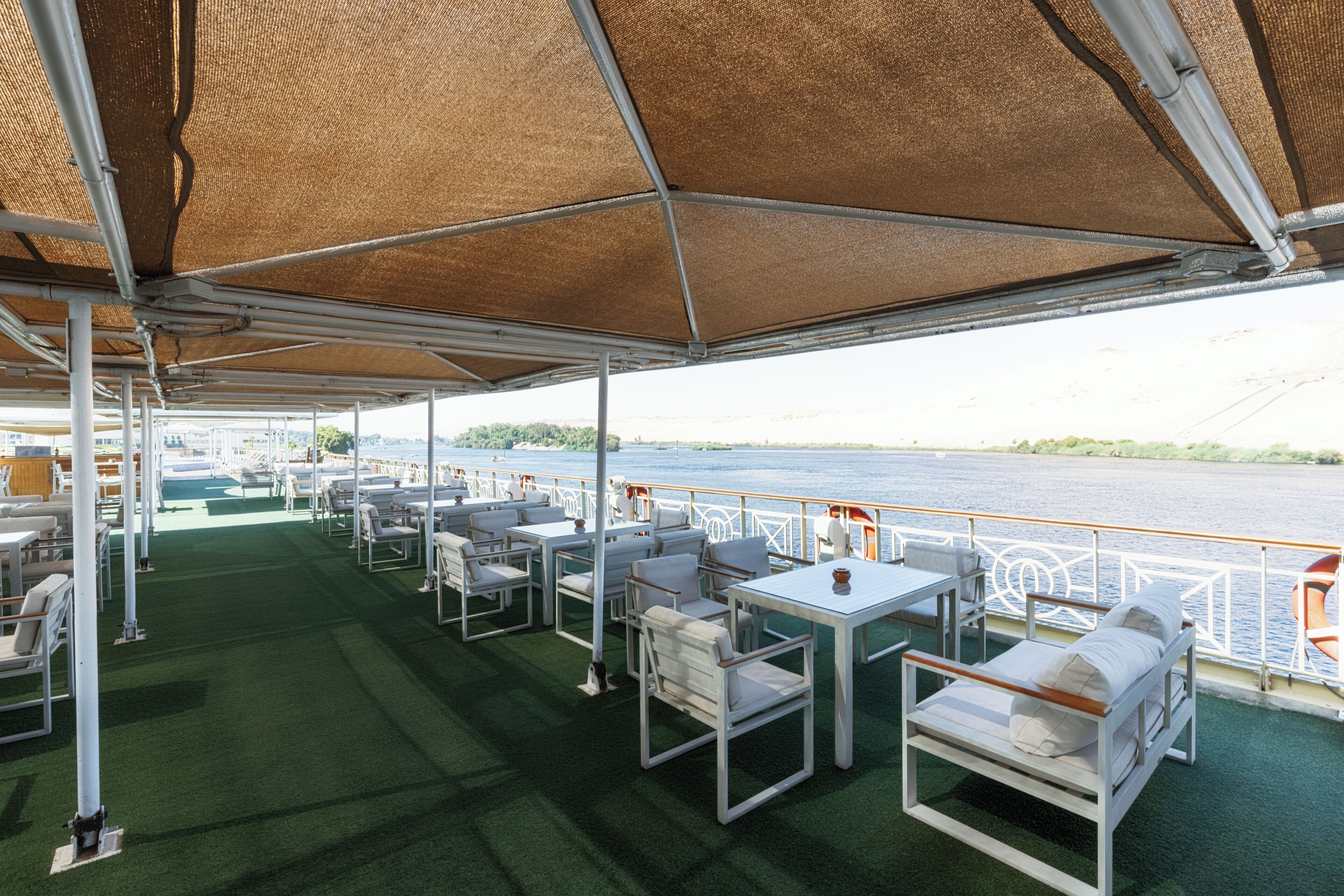 A covered outdoor seating area with tables and chairs, overlooking a body of water.