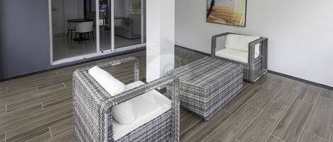 A modern outdoor seating area with wicker furniture and a glass door leading to a dining area.