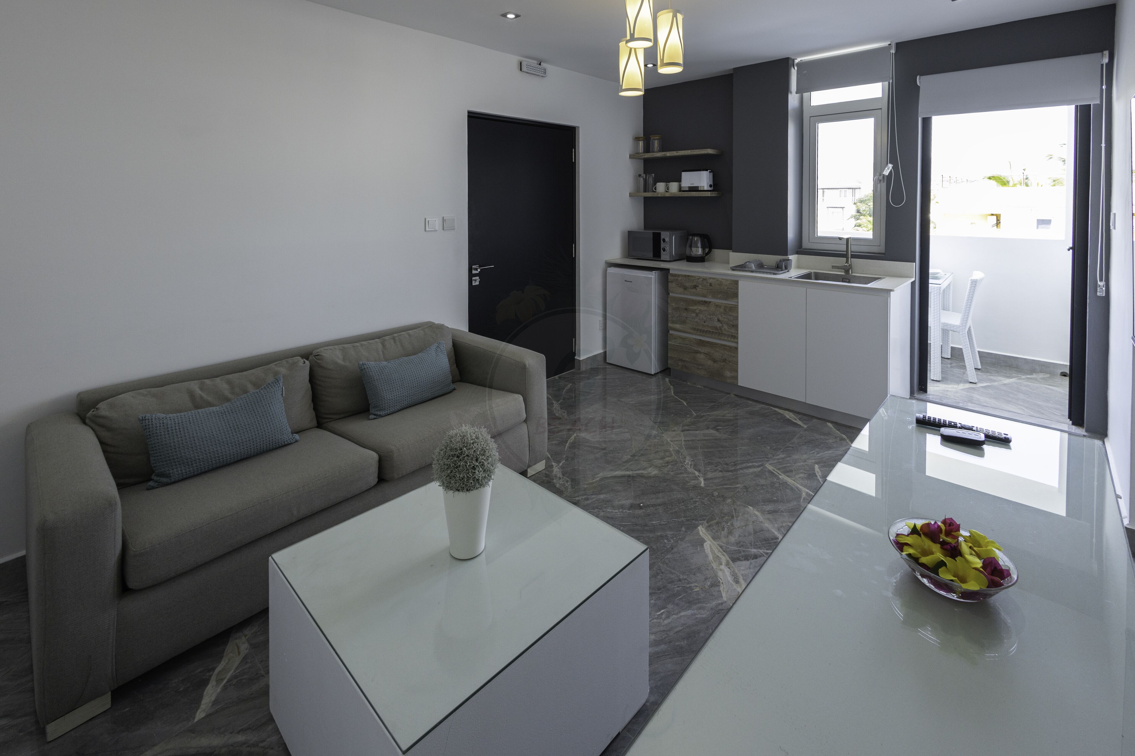 Una sala de estar moderna con un sofá, una mesa de centro y una cocina equipada con refrigerador, microondas y lavaplatos.
