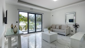 Una sala moderna con una mesa de comedor de vidrio, sofás blancos y un gran ventanal corredero que da a un balcón.