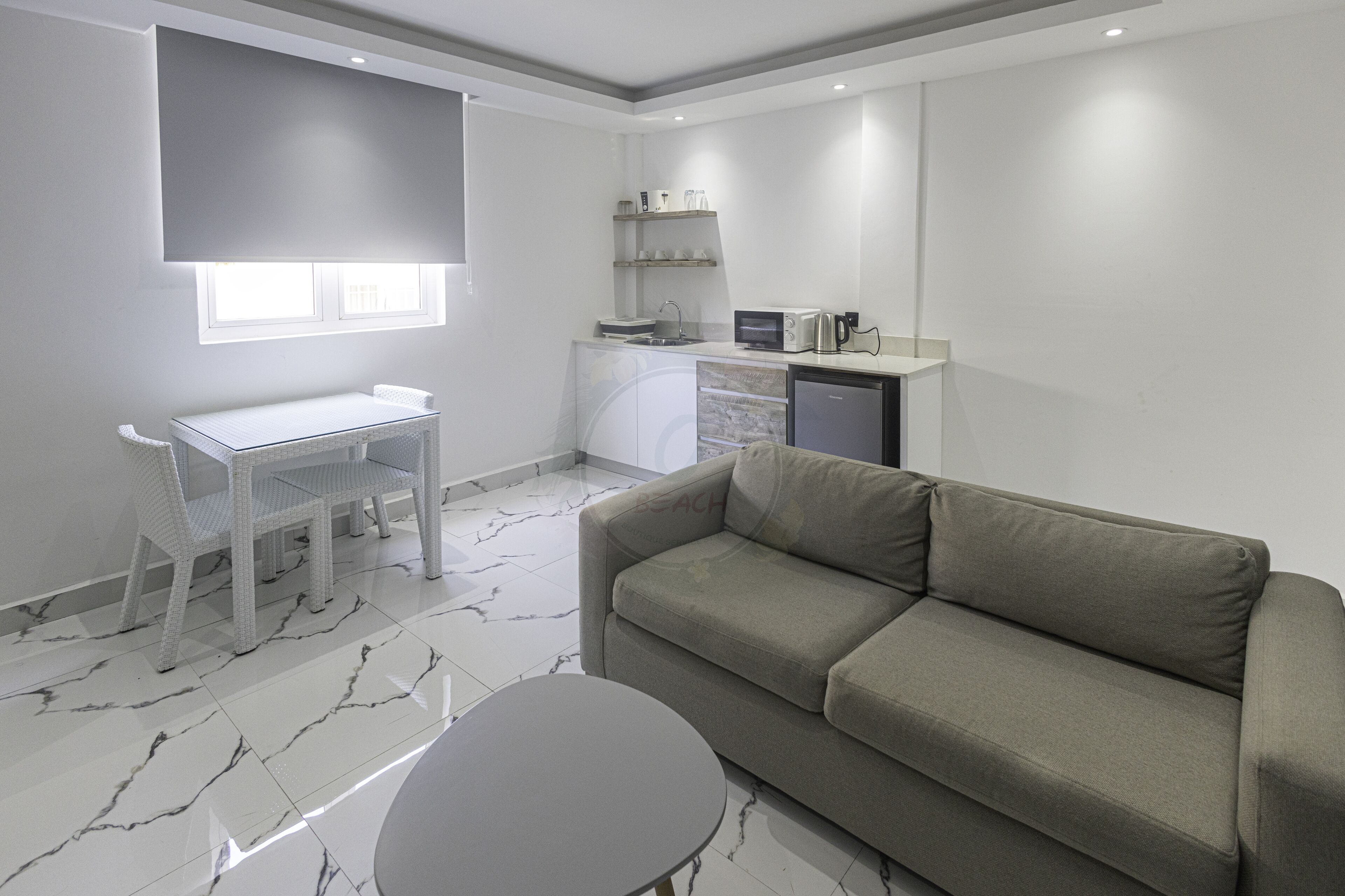 A modern kitchen with a built-in microwave, toaster, and coffee maker, a dining area with a white table and chairs, and a grey sofa.