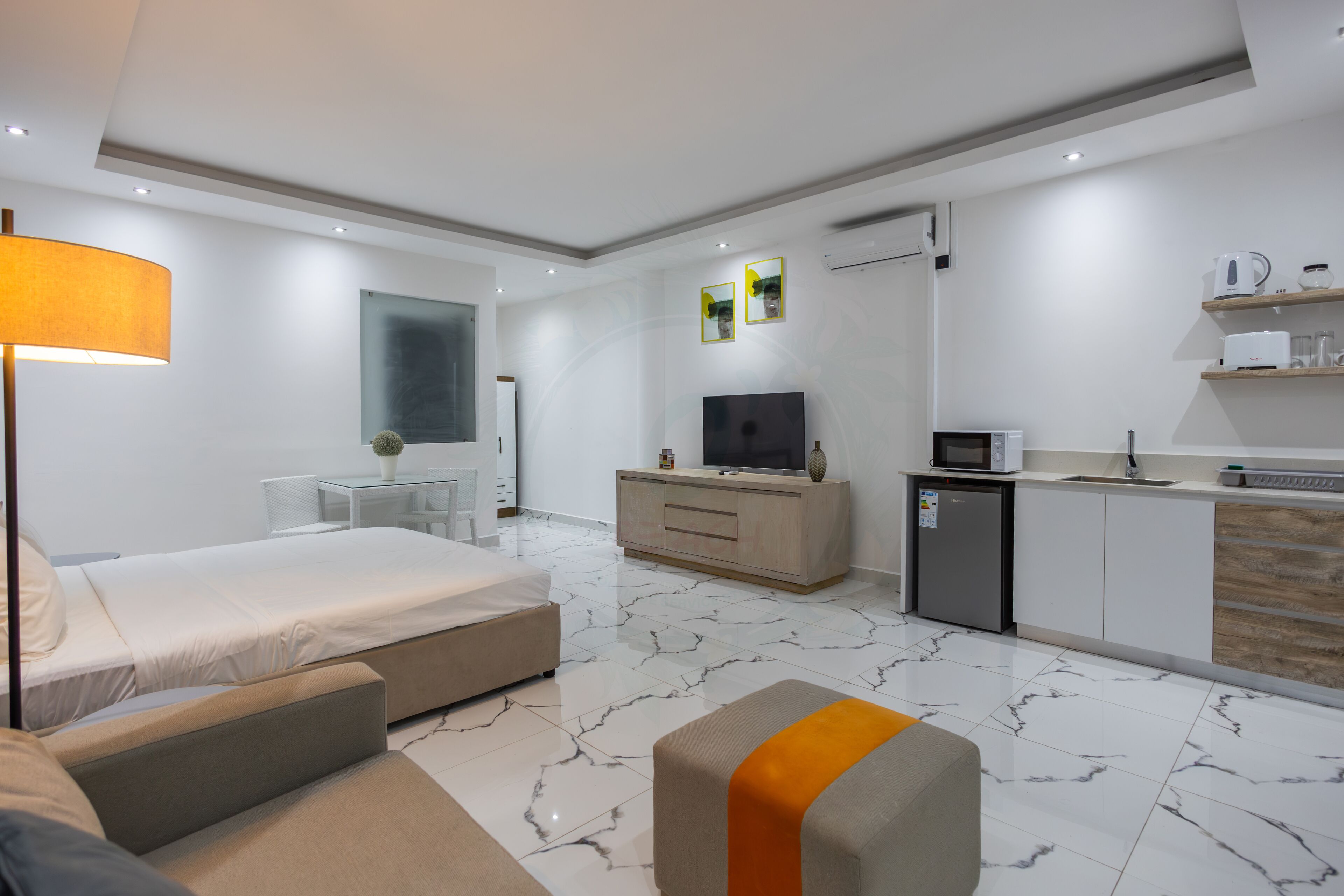 Et moderne hotelværelse med seng, sofa, fjernsyn, tekøkken og spiseplads.