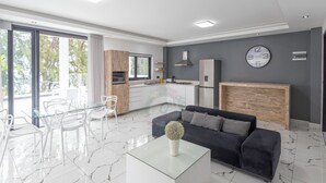Una sala de estar moderna con una mesa de centro de vidrio, un sofá oscuro y un comedor con sillas blancas.