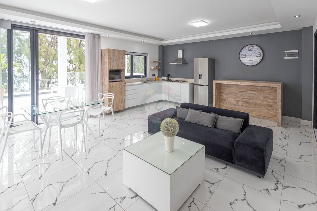 Ein modernes Wohnzimmer mit einem Glastisch, einem dunklen Sofa und einem Essbereich mit weißen Stühlen.