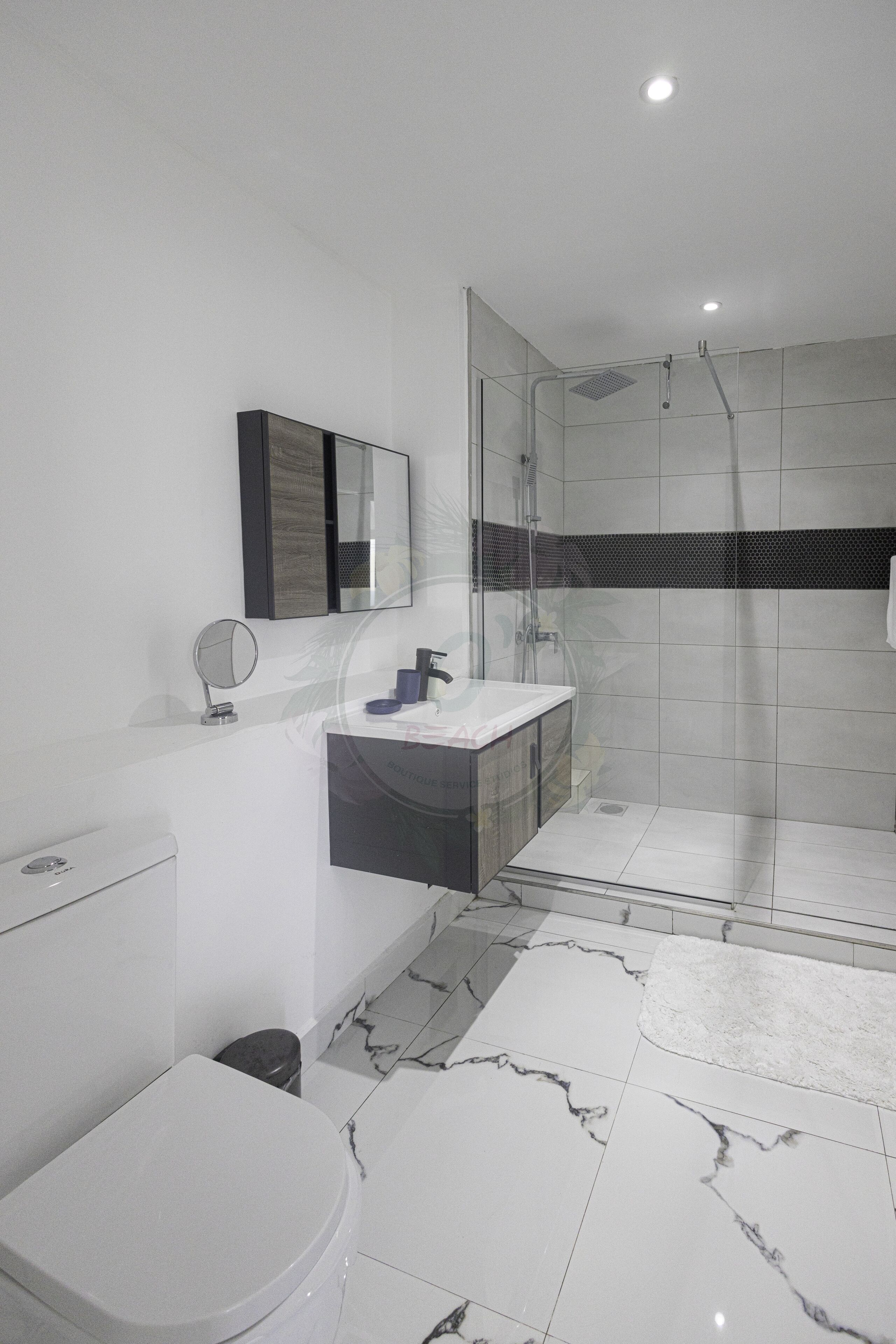 A modern bathroom with a glass-enclosed shower, a white toilet, a vanity with a mirror, and a marble-tiled floor.