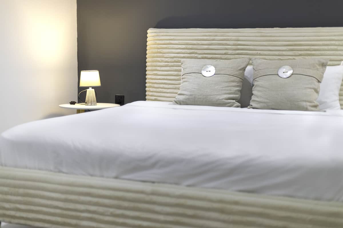 Ein ordentlich bezogenes Bett mit Kopfteil, einer Nachttischlampe und zwei Kissen mit runden Knöpfen.