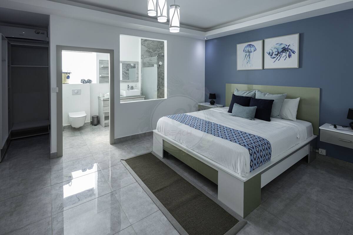 Ein modernes Schlafzimmer mit einem großen Bett, einem Nachttisch und Blick ins Badezimmer.
