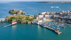 An aerial view of a coastal town with a prominent castle, a marina with numerous boats, and a mix of historic and modern buildings. - Min Y Mor - Breathtaking Sea Views (Tenby)