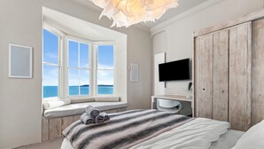 A bedroom with a large window, a bed, a TV, and a wardrobe. - Min Y Mor - Breathtaking Sea Views (Tenby)