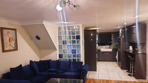 Ein Wohnzimmer mit einem blauen Sofa, einem Glastisch und einer Küchenzeile mit dunklen Schränken und einer Bartheke.