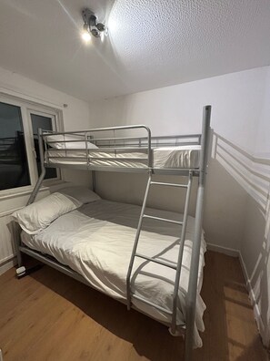 Dormitorio con literas, ventana, luz en el techo y suelo de madera.