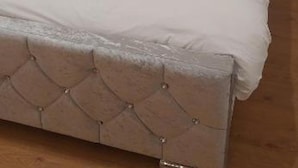 Ein Bett mit einem karrakten Kopfstück, weißer Bettwäsche und Holzboden.