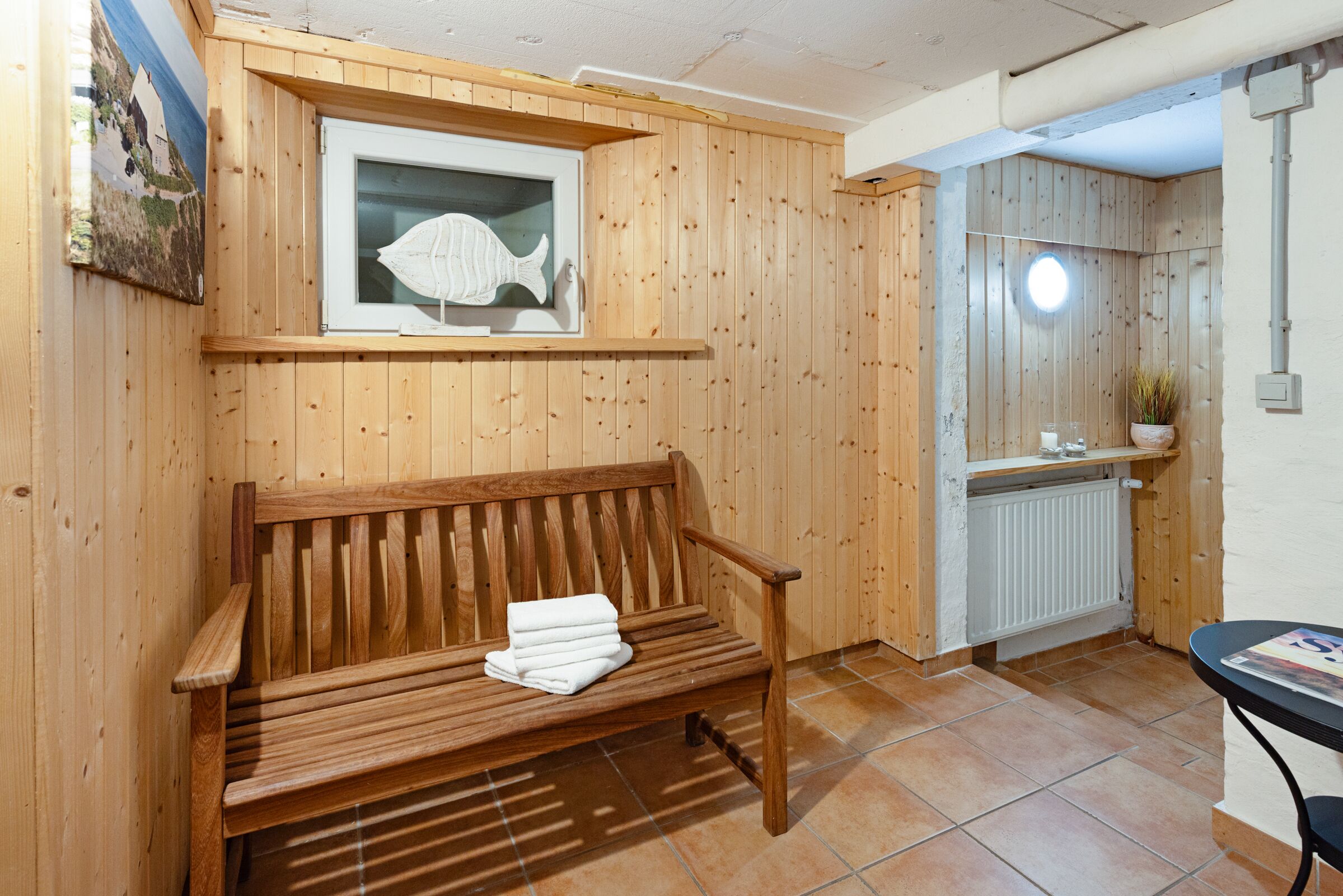 Um banco de madeira com uma toalha, um quadro de um peixe e um radiador em um quarto com paredes de madeira.
