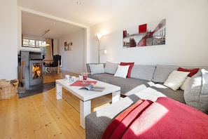 A modern living room with a fireplace, a sofa, a coffee table, and a dining area. - Herzlich Willkommen im Ferienhaus Haus am Heidetal (List)