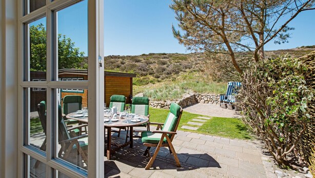Un patio al aire libre con una mesa dispuesta para comer, sillas verdes acolchadas y vistas a un paisaje natural.