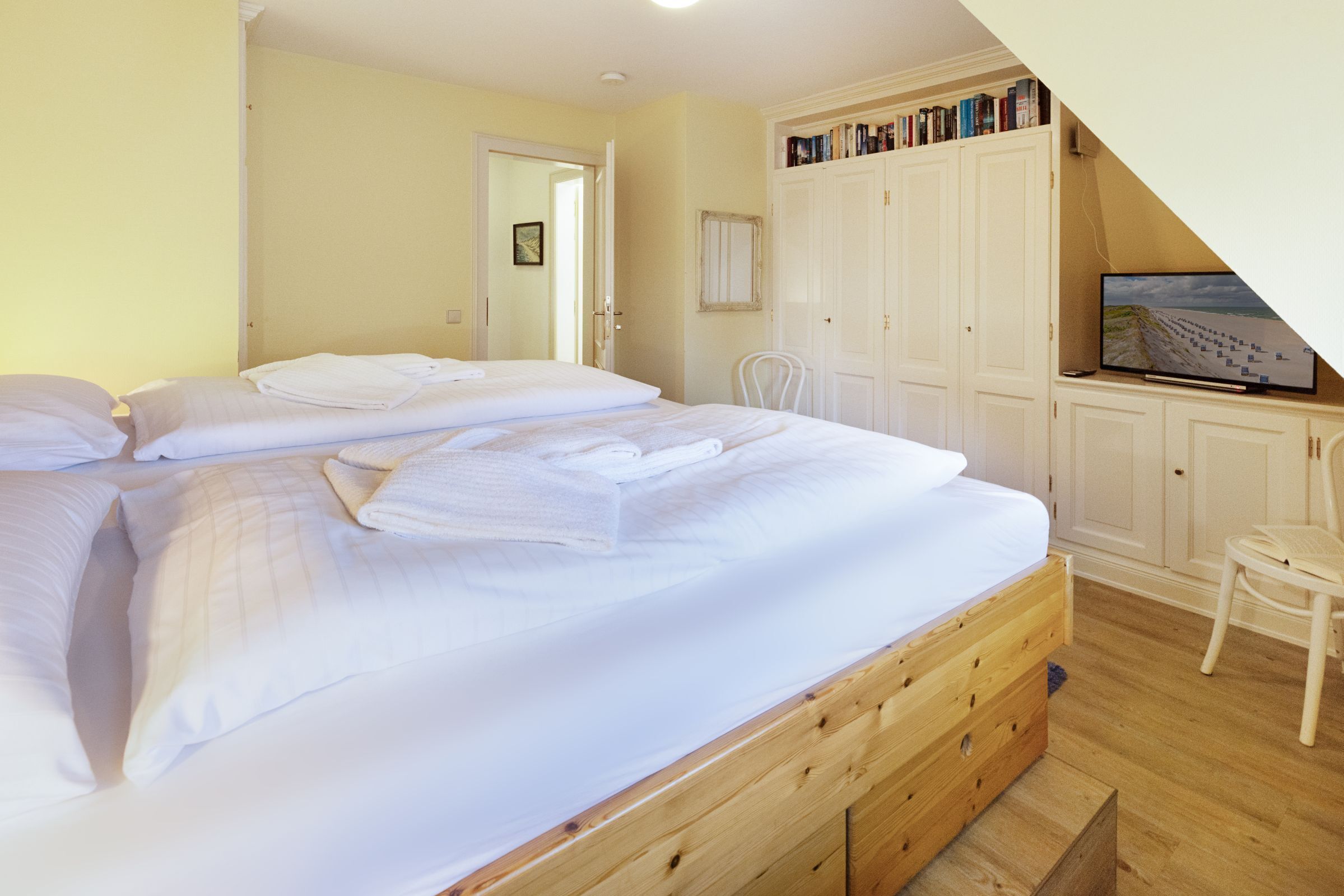 Een slaapkamer met twee bedden, een houten dressoir, een stoel en een televisie op een plank.