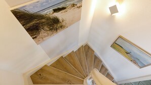 Un escalier en colimaçon avec des marches en bois, et au-dessus, un tableau représentant une scène de plage.
