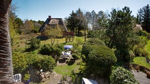 Une maison au toit de chaume, entourée d’un jardin bien entretenu où poussent différentes espèces d’arbres et d’arbustes.