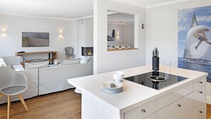 Une cuisine moderne dotée d’un îlot central, de meubles blancs et d’un coin repas avec un canapé et des chaises.