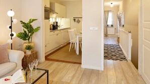 Una sala moderna con una mesa de centro de vidrio, un sofá y una planta. Se ve una cocina a través de una puerta abierta.