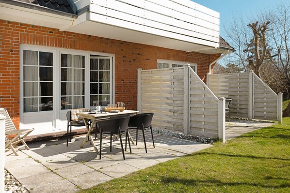 A patio with a table and chairs, a brick wall, and a white fence. - Herzlich Willkommen im Appartement Borlis Perle (List)