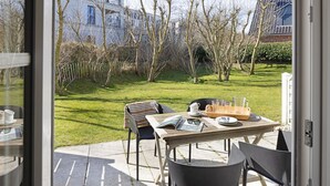 Un patio al aire libre con una mesa preparada para dos personas, sillas y vistas a un área verde con árboles y edificios al fondo.